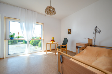 Einzelzimmer mit einem Pflegebett und großem Fenster